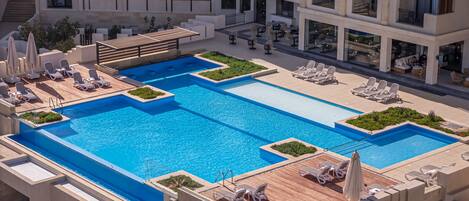 A rooftop swimming pool with multiple levels of balconies, lounge chairs, and a wooden deck area.