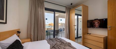 Habitación de hotel con cama, televisor, cómoda de madera y vistas a una piscina y zona de estar al aire libre.