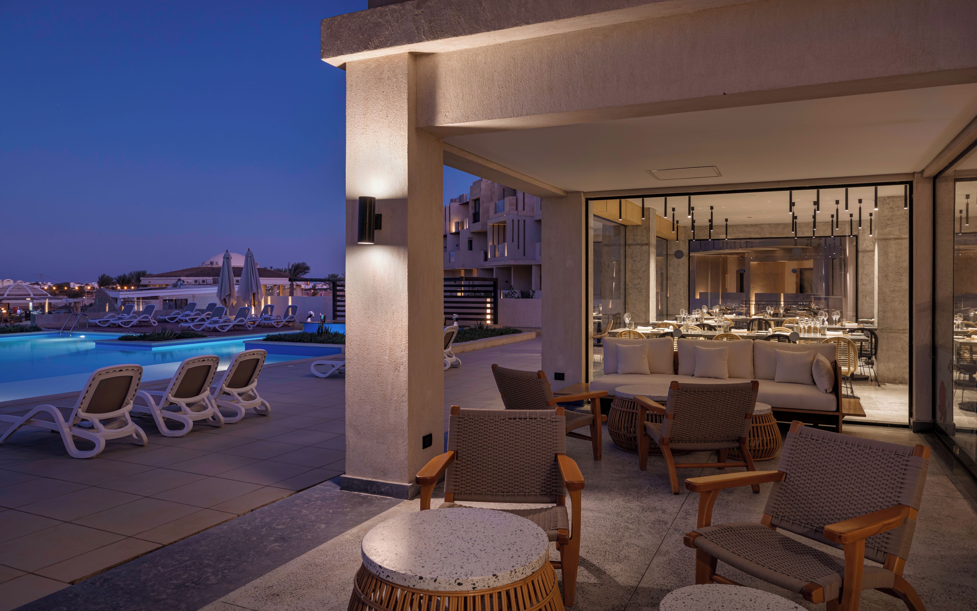 Un área de piscina en la azotea con sillones de descanso, un bar y un comedor con mesas y sillas.