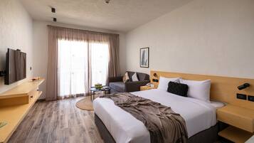 A hotel room with a large bed, a desk, a chair, a television, and a window with curtains.