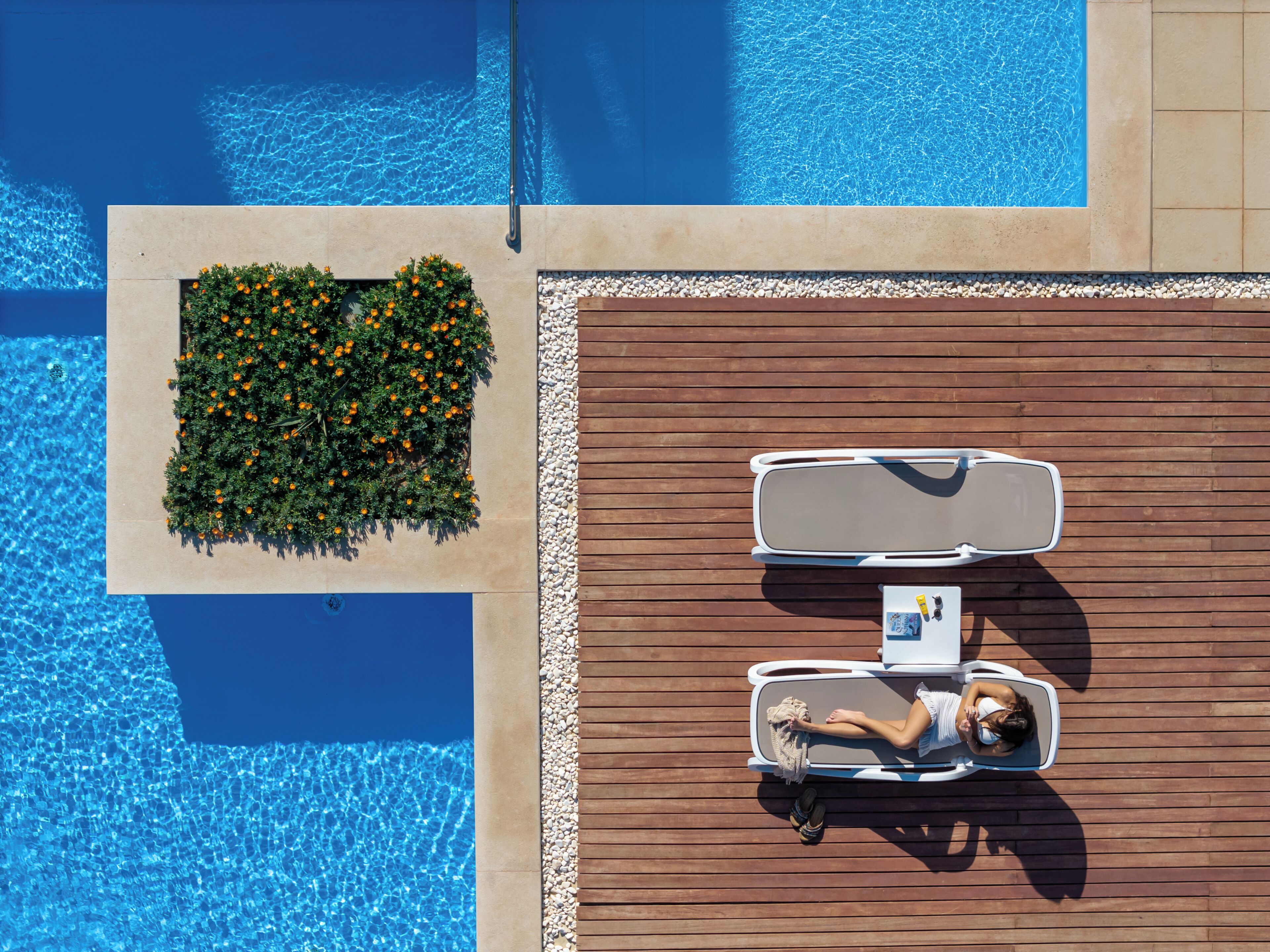 Vue aérienne d’une piscine dotée d’une terrasse en bois, de chaises longues et d’un petit espace jardin.