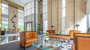 A spacious lobby with leather sofas, a glass coffee table, and a large window offering a view of greenery.
