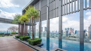 A rooftop infinity pool with a city view, surrounded by palm trees and modern architecture.