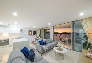 Una sala de estar moderna con un sofá, una mesa de centro y vistas a la puesta de sol a través de amplias puertas de cristal.