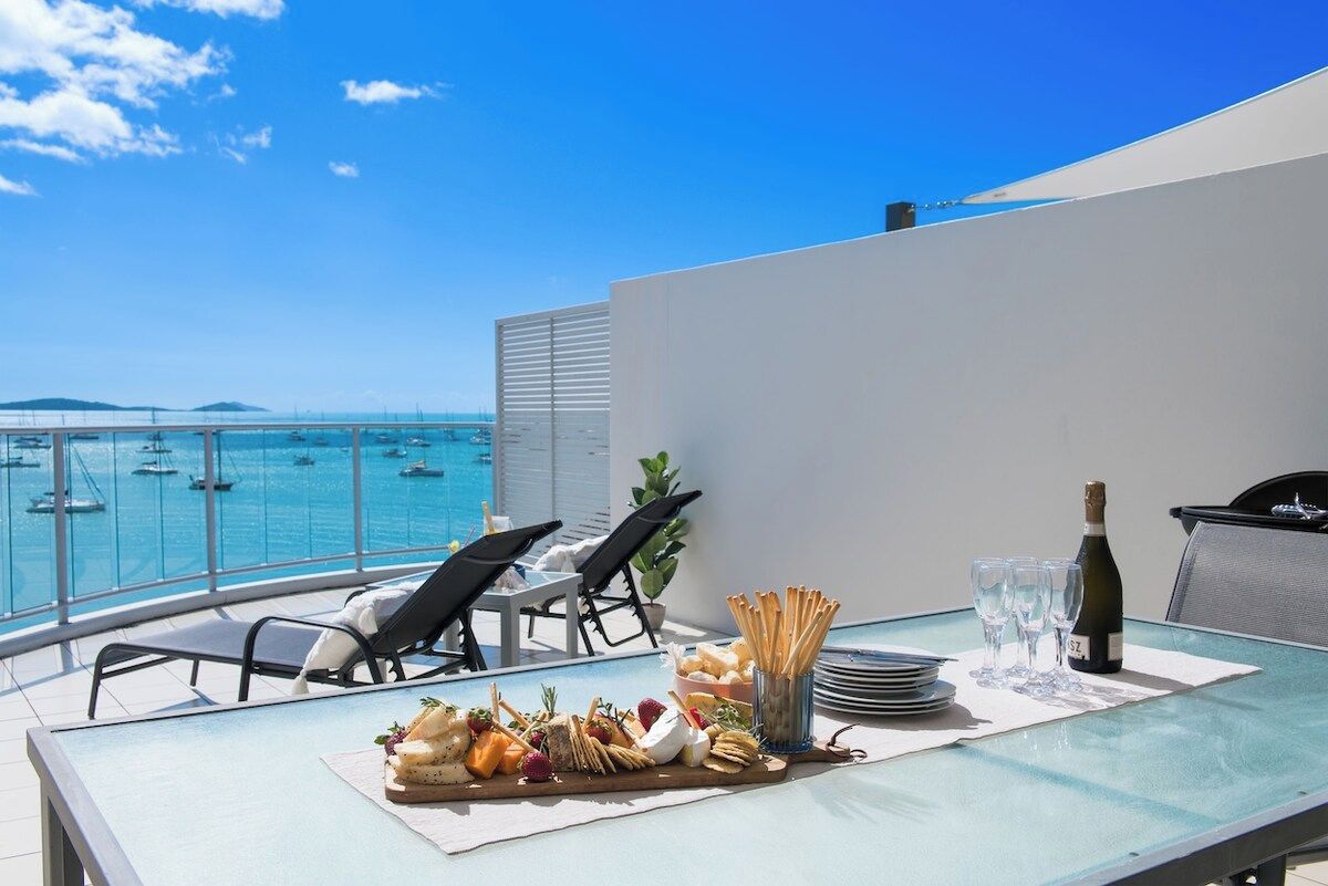 A balcony with a table set for a meal, overlooking a pool with boats.