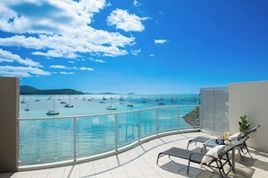 A balcony with a glass railing overlooking a marina with sailboats.