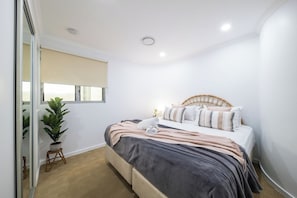 A bedroom with a bed, a window with blinds, a potted plant, and a ceiling light.