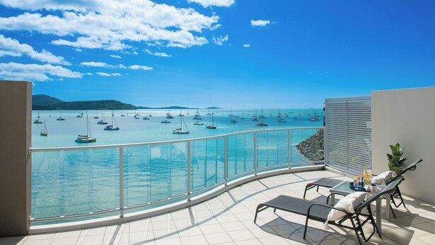 A balcony with a clear view of the sea and boats, a glass railing, and two lounge chairs. - Epitome of luxury - absolute waterfront penthouse (Cannonvale)