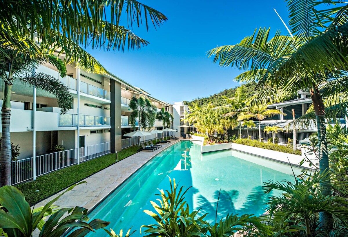 Un hôtel doté d’une piscine entourée de palmiers et situé dans un paysage vallonné.