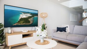 Una sala moderna con un televisor de pantalla plana, una mesa de centro redonda blanca, un sofá gris y una lámpara de pie.