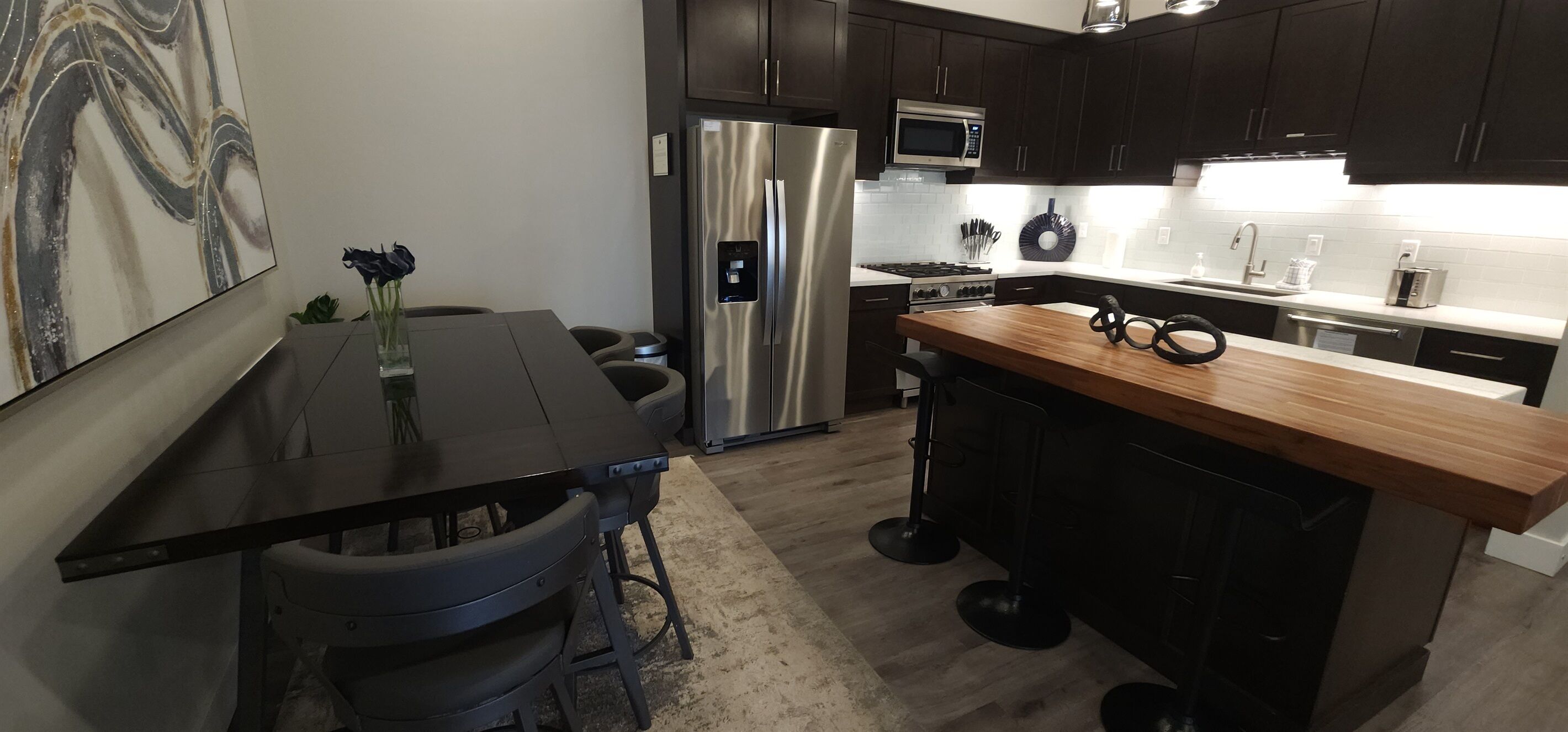 A modern kitchen with dark cabinets, stainless steel appliances, a wooden island, and a marble backsplash.