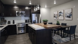 Una cocina moderna con armarios oscuros, electrodomésticos de acero inoxidable, una isla de madera y un comedor con sillas.