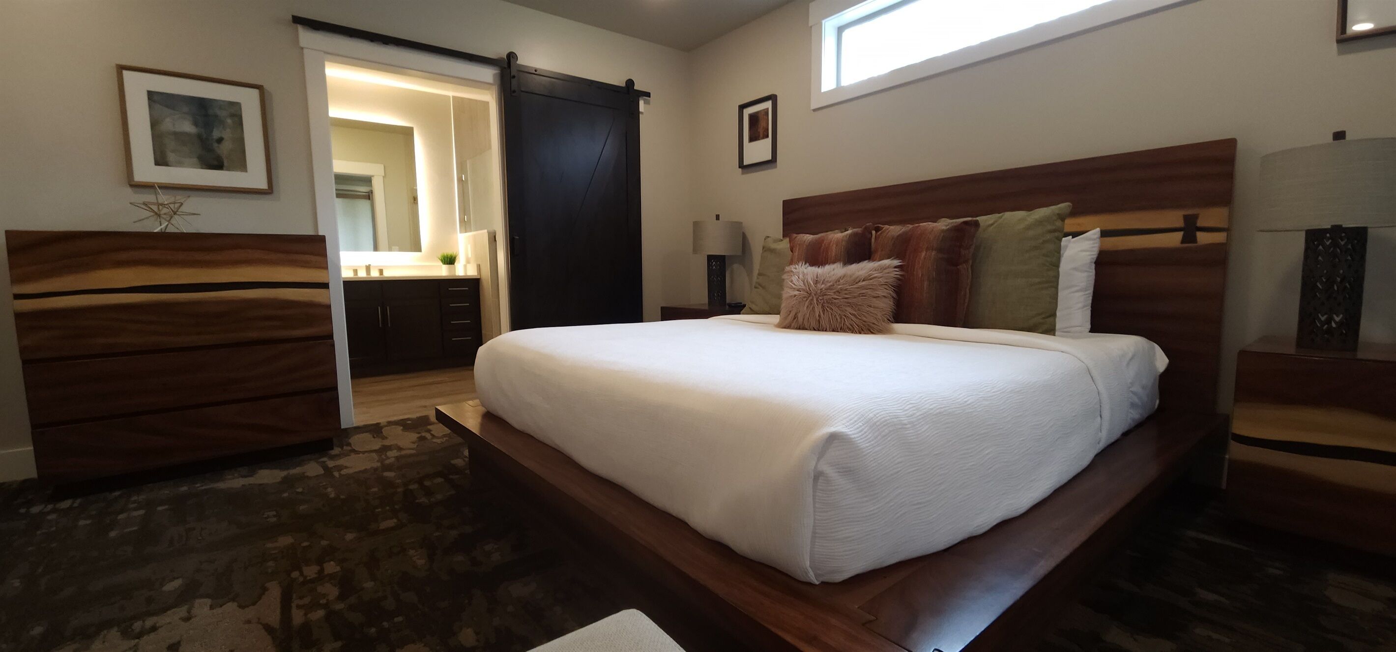 A bedroom with a large bed, a wooden dresser, a desk, a lamp, and a window.
