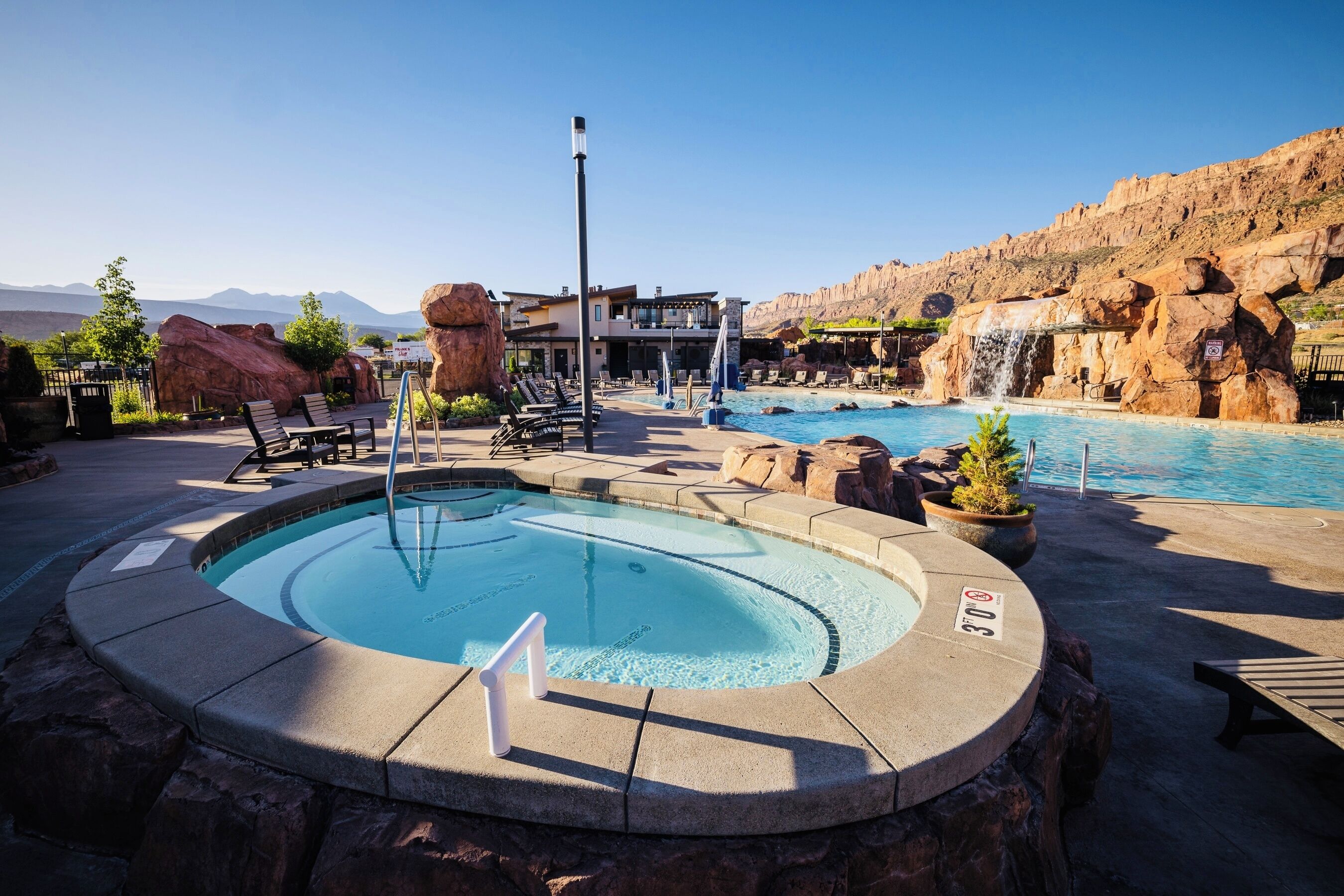 Un espace piscine avec des chaises longues, un jacuzzi et une vue sur les montagnes.