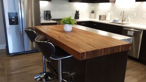 A modern kitchen with dark cabinets, stainless steel appliances, a wooden island with bar stools, and pendant lighting. - SageCreek E7 "BalancedRock Retreat" - Amazing Pool (Moab)