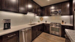 A modern kitchen with dark wood cabinets, a stainless steel dishwasher, a built-in microwave, and a gas stove. - SageCreek Moab Condo F11 - Stunning Pools/Hot Tubs (Moab)