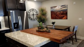 Cozinha moderna com bancada de granito, eletrodomésticos de aço inoxidável, mesa de jantar de madeira e pintura com paisagem desértica.