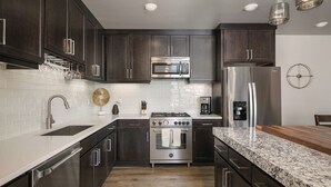 A modern kitchen with dark cabinets, stainless steel appliances, a granite countertop, and a wooden floor. - Sage Creek "Moab Reflections F2" - Stunning Pool (Moab)
