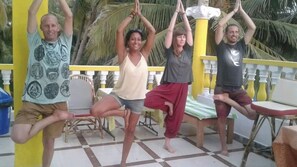 A group of people performing a yoga pose on a balcony with a checkered floor and yellow railing. - Cupids Heaven Resort (Canacona)
