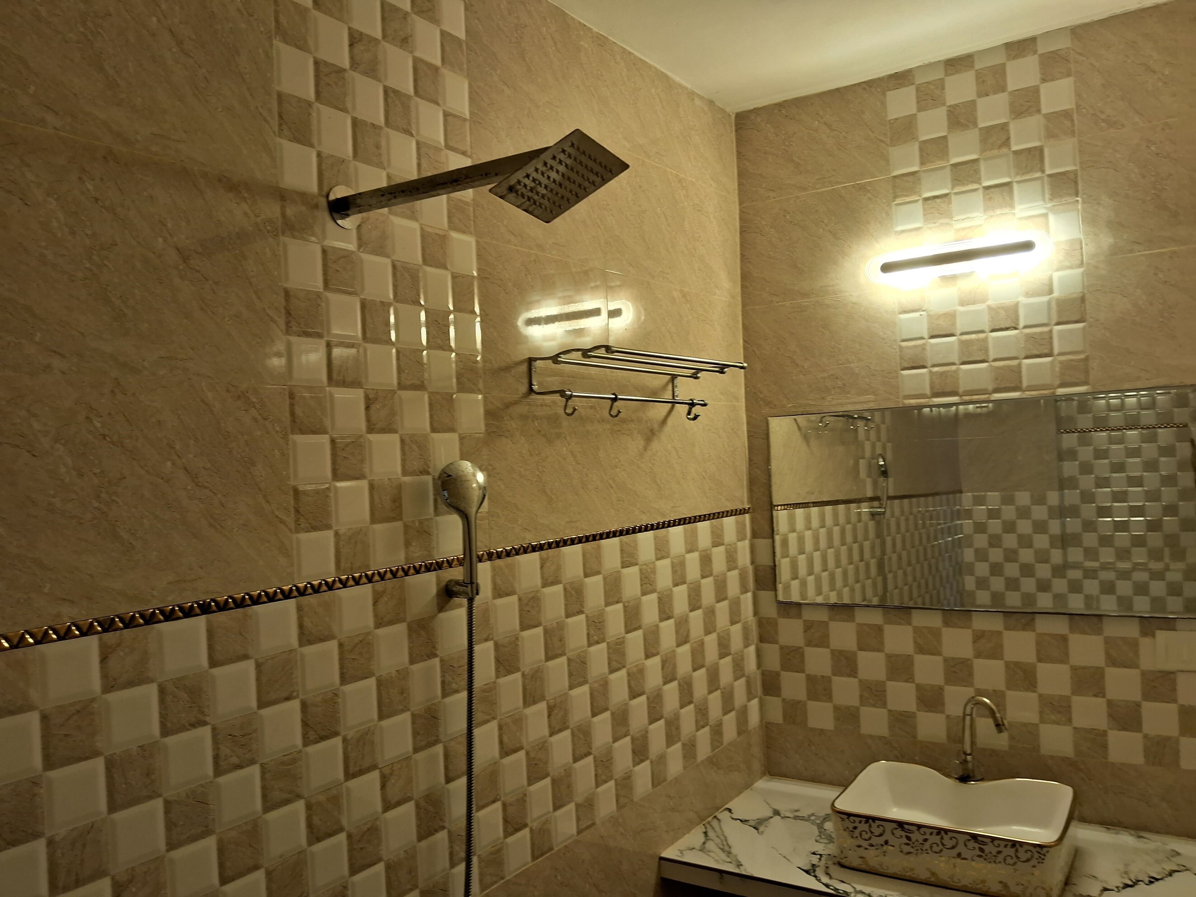 A bathroom with checkered tile walls, a shower with a handheld showerhead, a mirror, and a sink with a decorative basin.