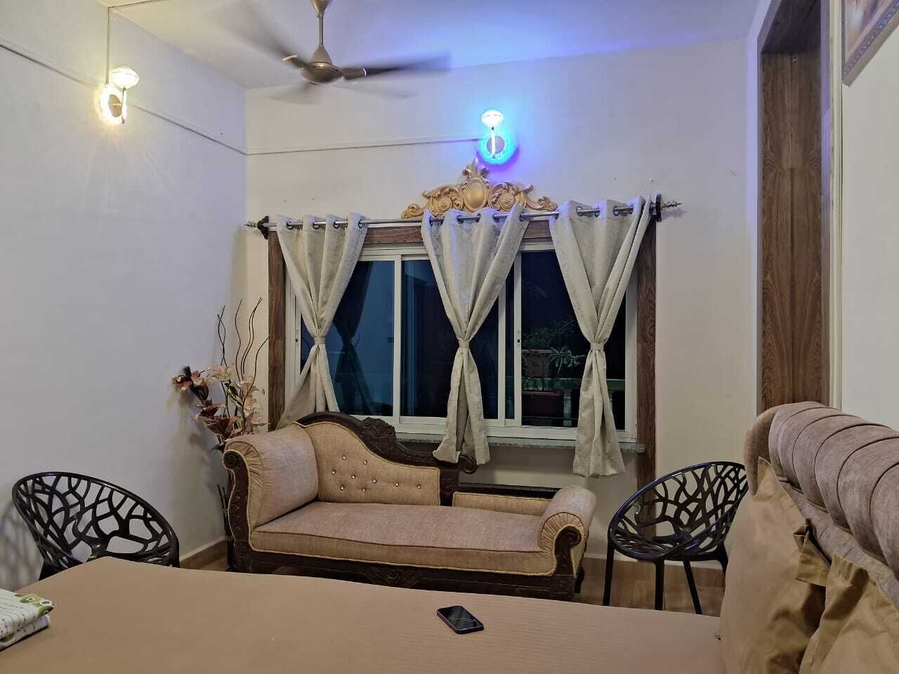 A cozy living room with a sofa, two chairs, a dining table, and a window with curtains.