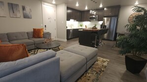 A modern living room with a grey sofa, orange cushions, a small round table, and a large potted plant.