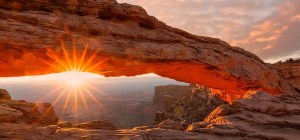 A natural rock formation with a sun shining through an arch.