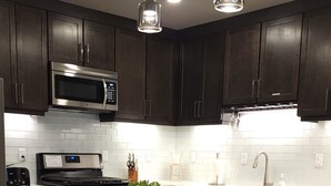 A modern kitchen with dark wood cabinets, stainless steel appliances, a wooden island, and pendant lighting. - Specials - F1,F2,F3,F4- Sage Creek Quad 1stFloor (Moab)