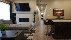 A modern living room with a sofa, a coffee table, and a TV. There is a kitchen area with a bar stool and a painting on the wall. - Sage Creek at Moab "Combo F10 & F11" Heated Pool (Moab)