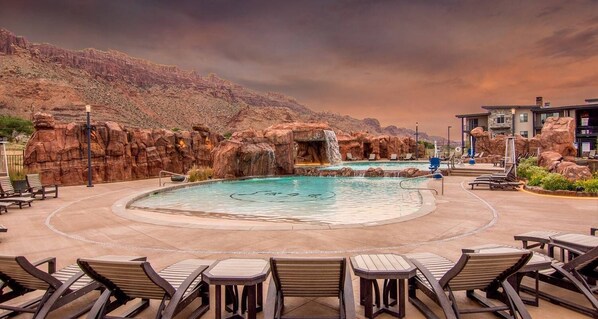 A pool area with a circular design, surrounded by lounge chairs and tables, with a mountainous backdrop. - Sage Creek at Moab "Combo F10 & F11" Heated Pool (Moab)