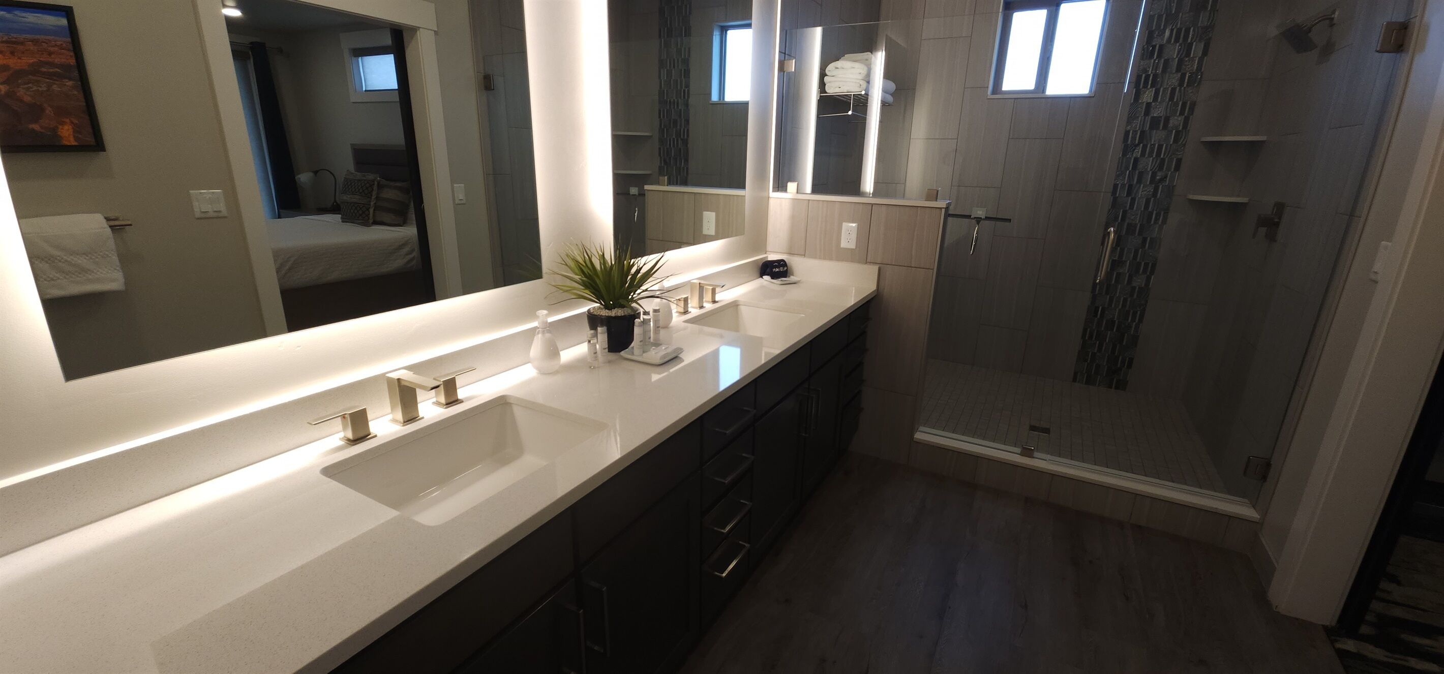 A modern bathroom with a large mirror, a sink, a shower, and a potted plant.