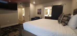 Une chambre avec un grand lit, un téléviseur à écran plat fixé au mur, une porte de couleur sombre et un miroir au-dessus du lit.