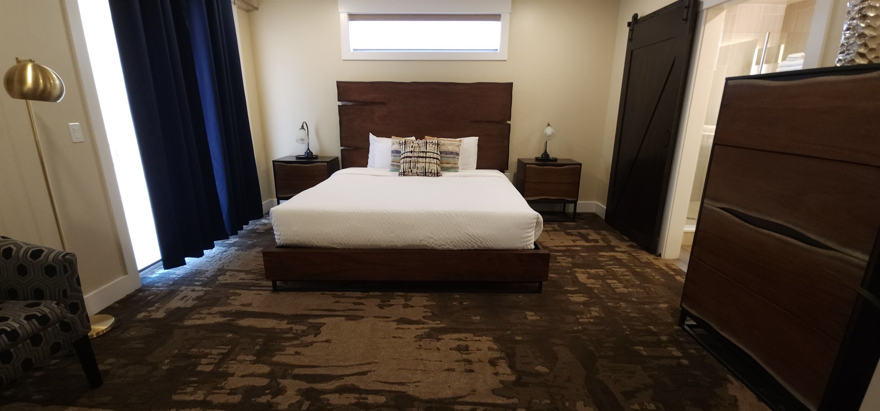A bedroom with a large bed, two bedside tables, a dresser, and a patterned carpet.