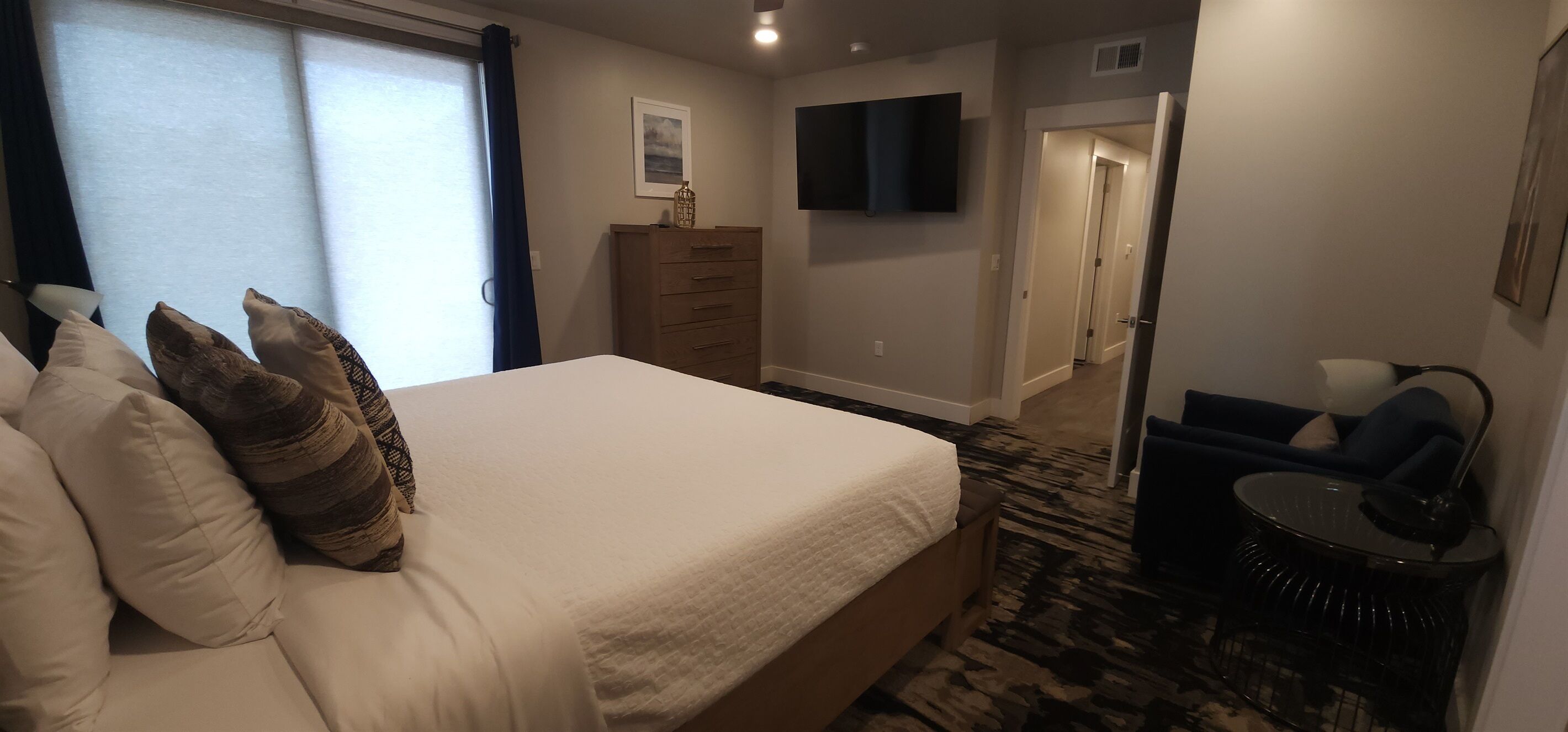 Camera d'albergo con un letto grande, una cassettiera, una TV a muro e un piccolo angolo relax con una sedia e un tavolino.