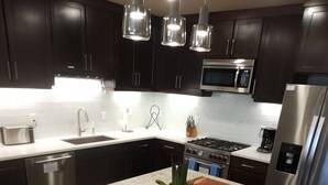 A modern kitchen with dark cabinets, stainless steel appliances, a wooden island with bar stools, and pendant lighting. - Sage Creek Resort at Moab - Quad Rental F5-6-7-8 (Moab)