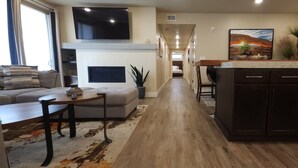 A modern living room with a sofa, coffee table, and TV. A kitchen area with dark cabinets and a countertop is visible. - Sage Creek Moab "Dual Unit Rental" F6 & F7 (Moab)