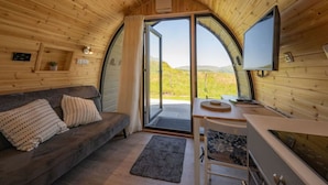 A cozy cabin interior with a wooden ceiling, a sofa with patterned cushions, a small table, and a TV.