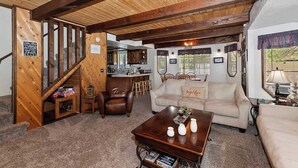 Ein gemütliches Wohnzimmer mit einer Holztreppe, einem Essbereich und einer im Hintergrund sichtbaren Küche.