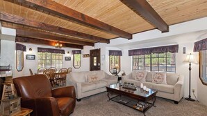 Ein gemütliches Wohnzimmer mit Holzbalkendecke, zwei Sofas, einem Couchtisch und einer Essecke mit Stühlen und Tisch.