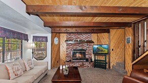 Ein gemütliches Wohnzimmer mit Kamin, Holzbalken, einer Couch und einem Couchtisch.