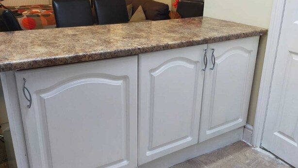 Una cocina con armarios blancos, encimeras de granito y piso de baldosas.