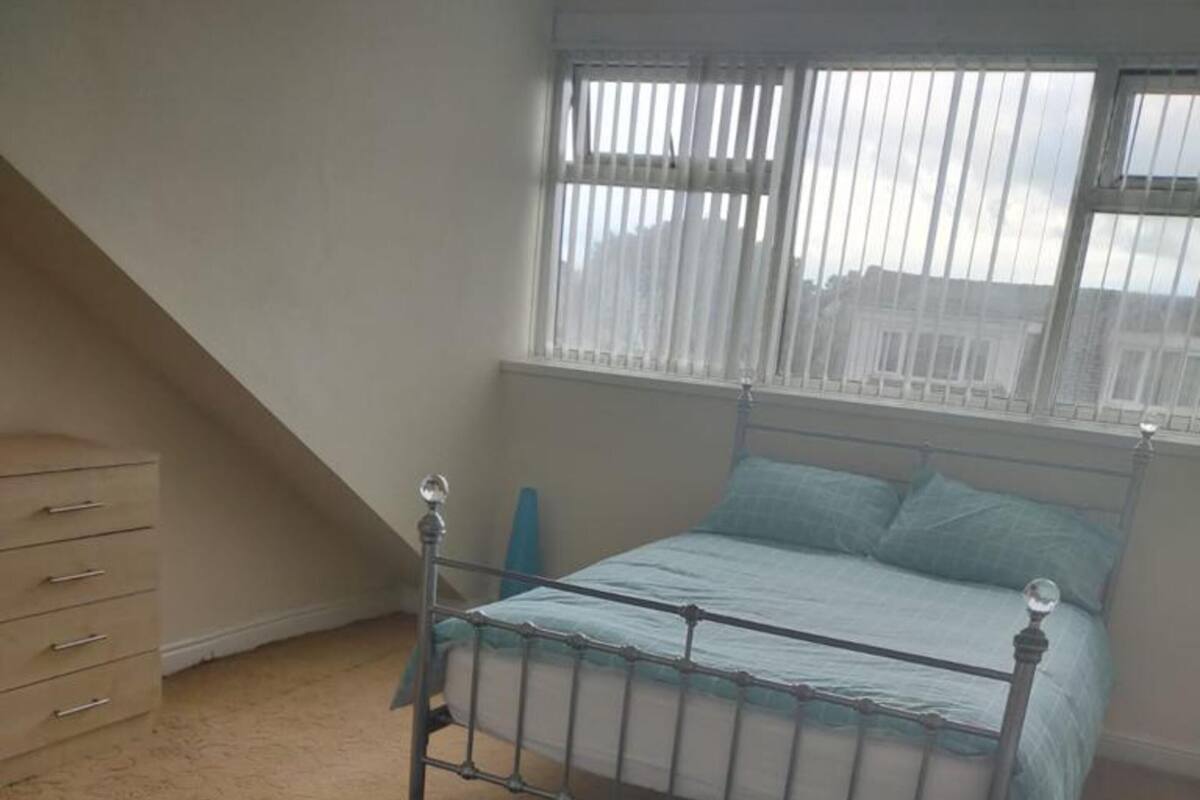 A bedroom with a bed, a dresser, and a window with blinds.
