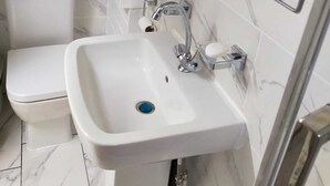Un baño con inodoro y lavamanos blancos, y un espejo con marco de metal.