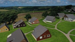 An aerial view of a residential area with houses, green lawns, and a hilly landscape in the background. - Coombe View Cornwall Holiday Lodge Near Bude. Sea Views. Large Patio Sleeps 6. (Kilkhampton)