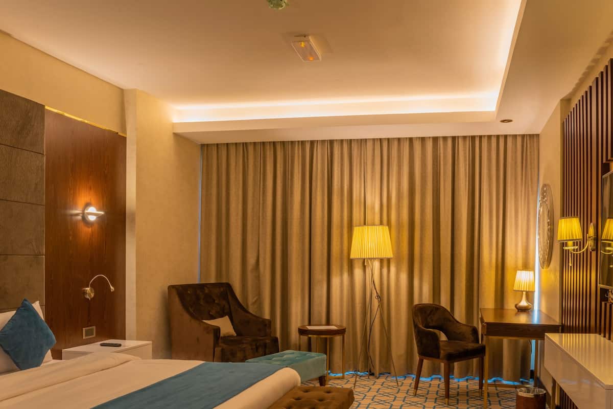 Habitación de hotel con una cama, dos sillas, un escritorio, una lámpara, un espejo y una cortina.
