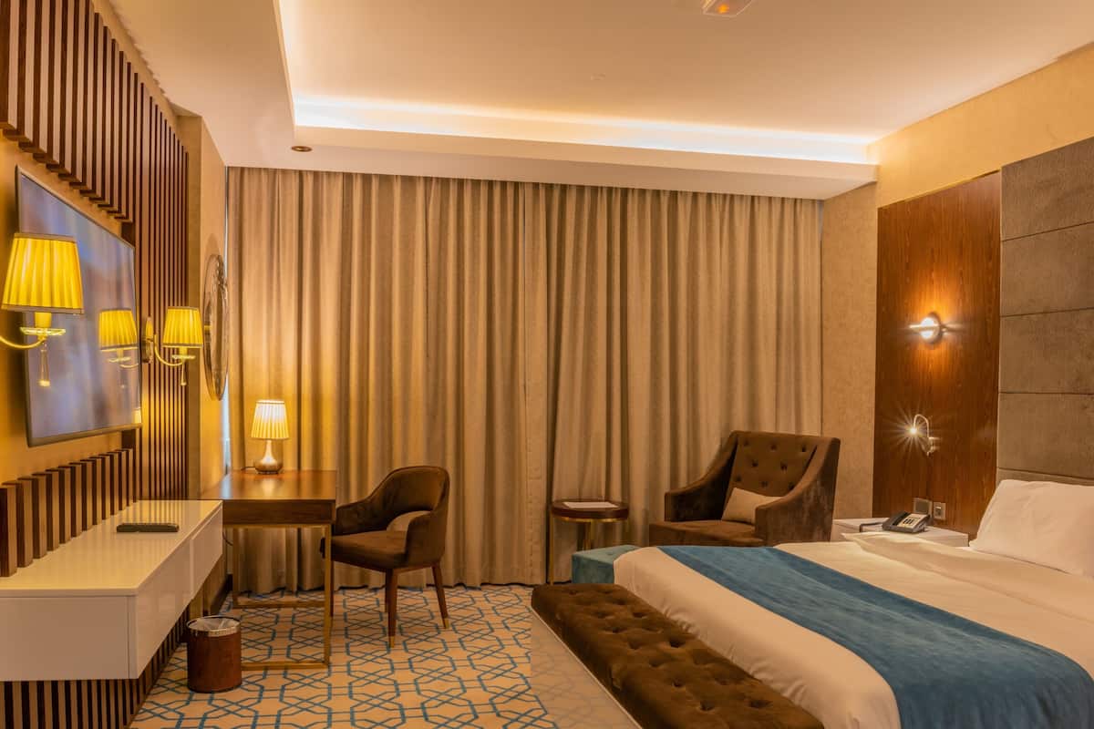 Una habitación de hotel con una cama, un escritorio con silla, una mesita, una lámpara y un televisor montado en la pared.