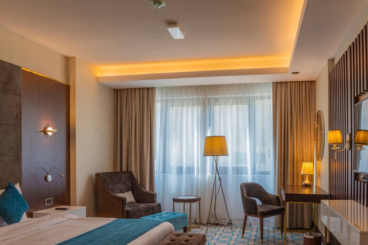 Una habitación de hotel con una cama grande, dos sillones, un escritorio, una lámpara y un espejo.