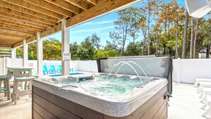 Ein Whirlpool unter einer Holzpergola, im Hintergrund ein Schwimmbecken.