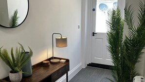 A hallway with a wooden console table, a floor lamp, and two potted plants. - The Lugger Inn (Fowey)