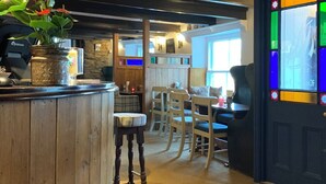 A cozy restaurant interior with wooden furniture, a bar area, and a colorful stained glass window. - The Lugger Inn (Fowey)